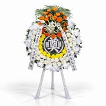 Corona funeraria sobre trípode con crisantemos blancos y amarillos, lirios blancos y gerberas naranjas.