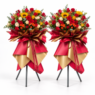 Dos composiciones de rosas y girasoles sobre trípodes para una inauguración, con envoltorio rojo y dorado.